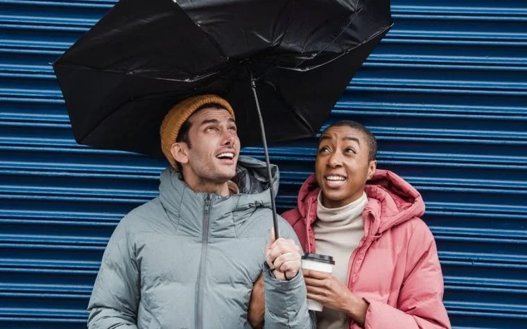 multiethnic friends with coffee under broken umbrella in windy weather